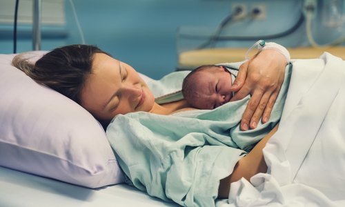 Photograph of a mother in a hospital bed holding a newborn